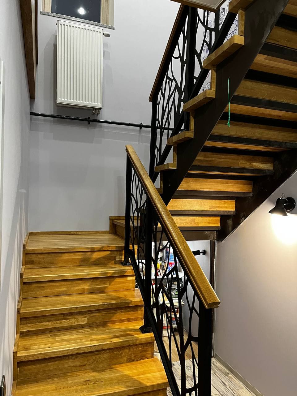 Modern wooden staircase with black metal railings featuring a decorative laser-cut branch pattern.