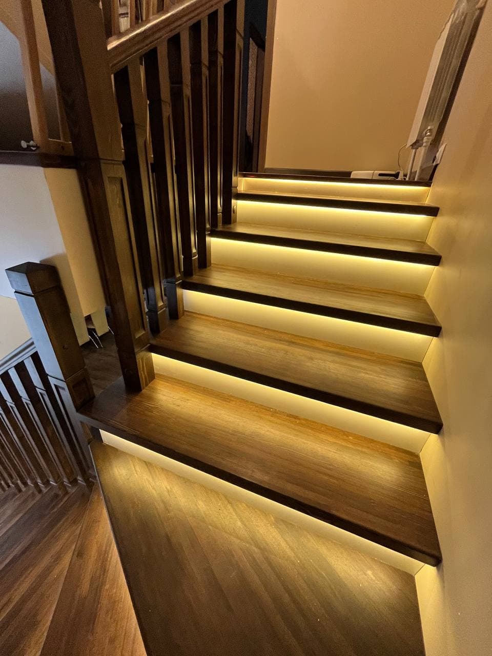 Dark wooden staircase featuring warm LED strip lighting installed underneath each step tread.